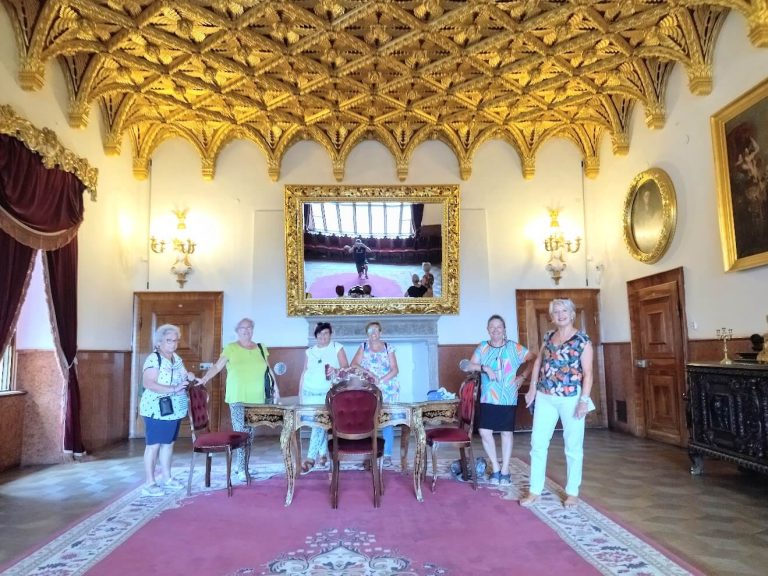 A group of visitors standing in a historic room with a richly decorated golden ceiling, elegant furniture, and ornate mirrors, showcasing the grandeur of Slovak heritage.