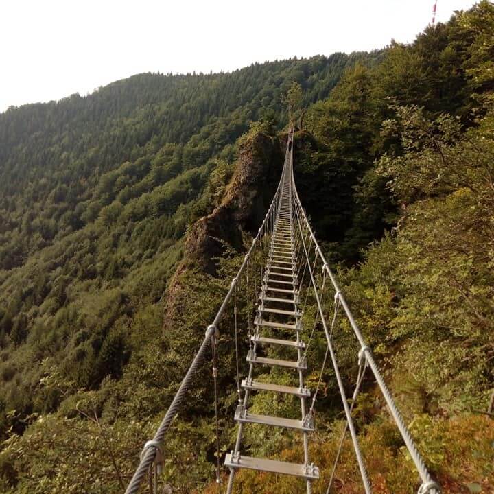 A narrow suspension bridge stretching across a lush green mountain ridge near Kremnica, offering a thrilling hiking experience