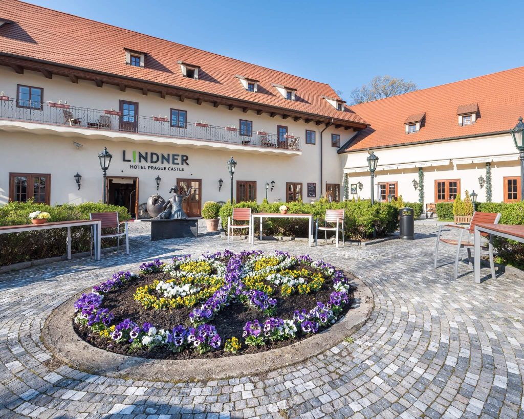 Courtyard of Lindner Hotel Prague Castle with blooming flowers and historical architecture on a sunny day.