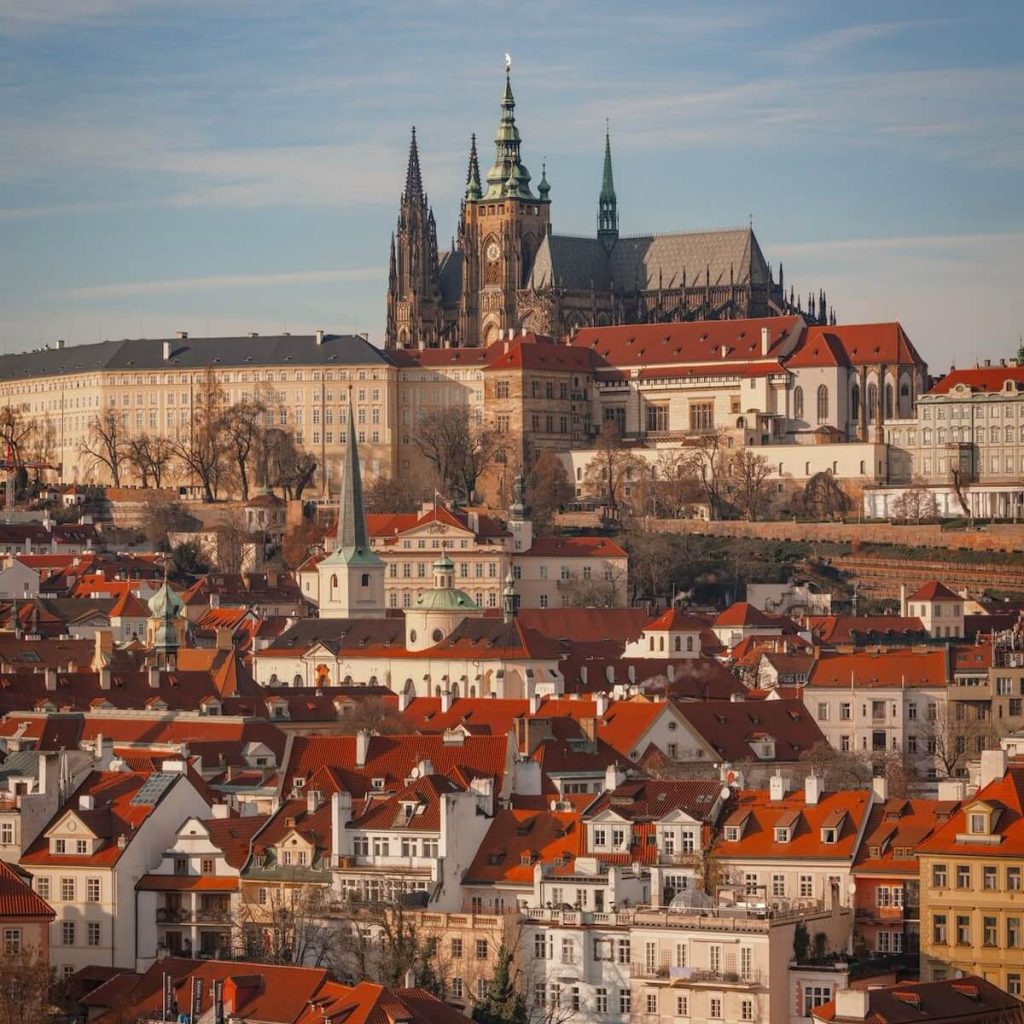 Panoramic view of Prague Castle and the red rooftops of the Lesser Town in Prague during golden hour.
