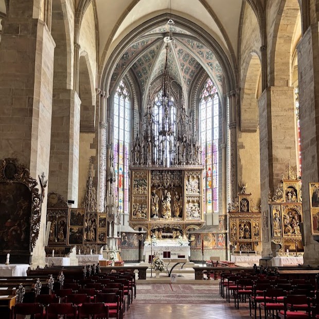 Interior of the Basilica of St. James in Levoča, Slovakia, showcasing the world’s tallest Gothic wooden altar by Master Paul of Levoča, surrounded by stained glass windows and richly decorated side altars.