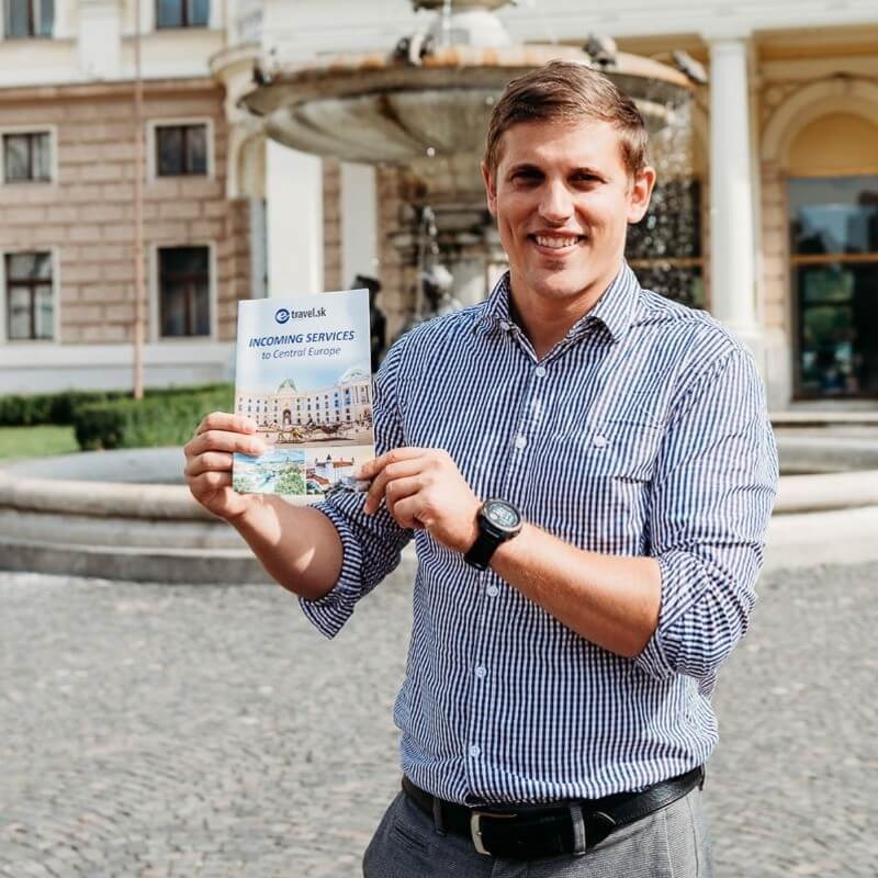 E-TRAVEL.SK DMC guide Andrej Stanik holding an Incoming Services to Central Europe brochure in front of a historic fountain in Slovakia