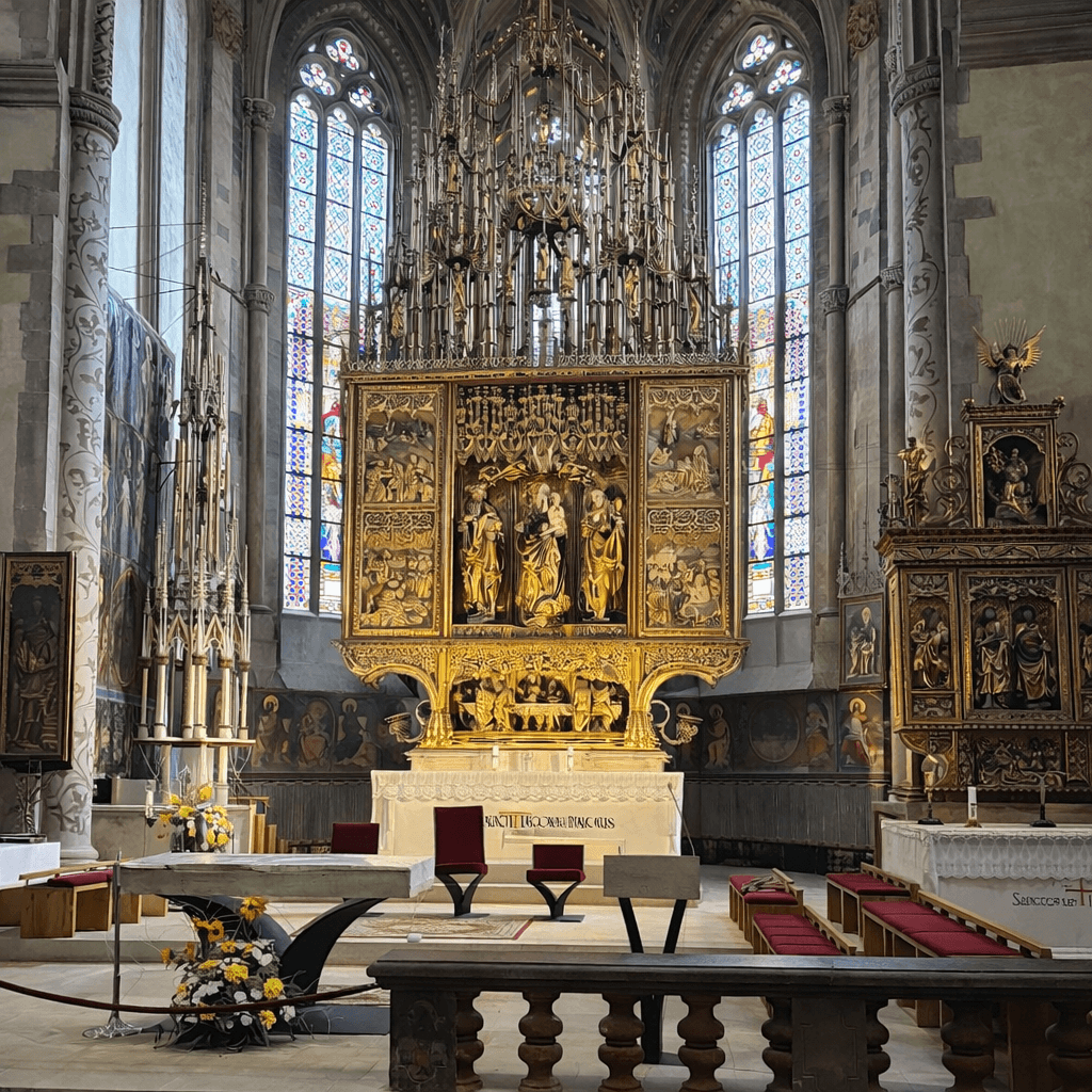 Interior of the Basilica of St. Jacob in Levoča, Slovakia, featuring the Gothic wooden altar of Master Paul of Levoča — the tallest Gothic wooden altar in the world at 18.62 metres — with gilded carved figures, colourful stained glass windows and side altars visible in the background.