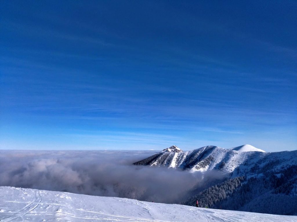 Snowy piste above a sea of clouds with a pyramid-shaped peak rising through the inversion at a Slovak ski resor