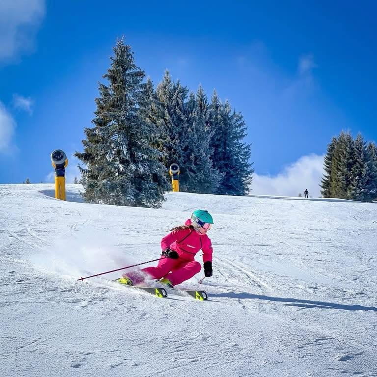 Skier in a pink suit carving a turn on a groomed piste at Malinô Brdo ski resort near Ružomberok, Slovakia